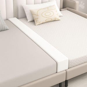 Peut inclure: Un cadre de lit beige avec une tête de lit blanche et une protection en mousse blanche. Le lit a deux matelas, un beige et un blanc avec un motif à pois. Des oreillers blancs et beiges avec un motif décoratif sont sur le lit.