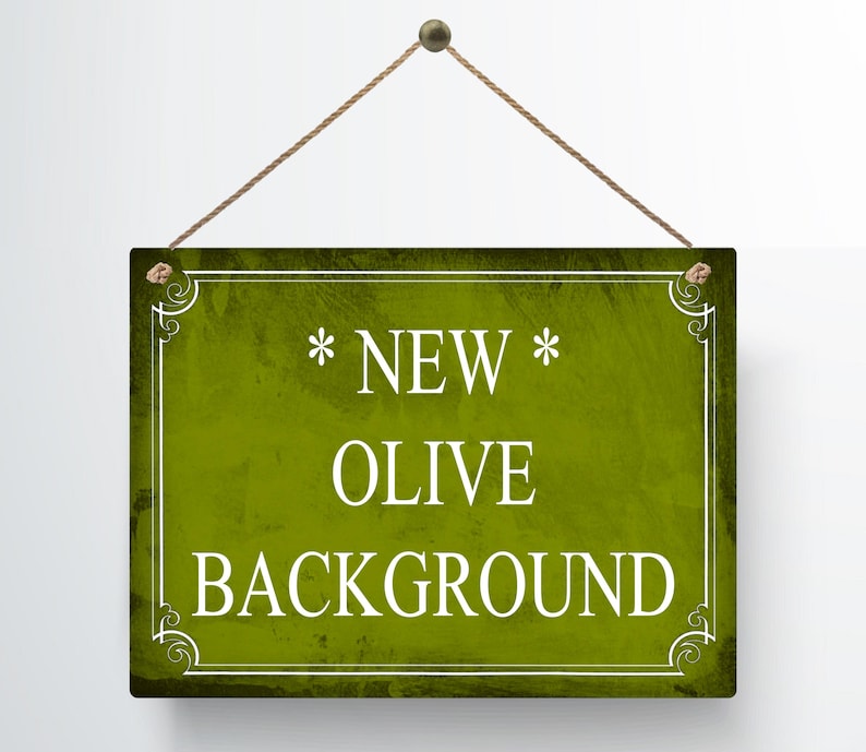 May include: A rectangular sign with an olive green background and white text that reads "* NEW * OLIVE BACKGROUND". The sign is framed with a white border and decorative corner elements. It hangs from a brown rope.
