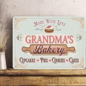 May include: A vintage-style sign with the text "Made with Love Always Fresh Grandma's Bakery Cupcakes Pies Cookies Cakes" in pink and brown lettering on a light blue background. The sign features a decorative border and a small illustration of a cake with pink frosting.