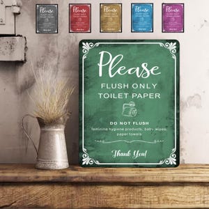 Könnte beinhalten: Ein grünes Schild mit weißem Text, auf dem steht: „Bitte nur Toilettenpapier spülen“. Das Schild besagt auch „Nicht spülen“ gefolgt von einer Artikelliste. Ein Metallkrug mit getrocknetem Gras steht auf einer Holzoberfläche.