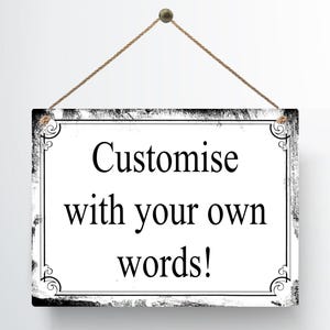 May include: A rectangular sign with a white background and black decorative border. The sign is suspended by a brown string and features the text "Customise with your own words!" in black.