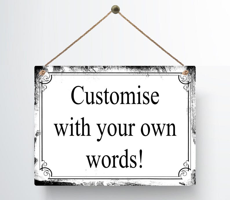 May include: A rectangular sign with a white background and black decorative border. The sign is suspended by a brown string and features the text "Customise with your own words!" in black.