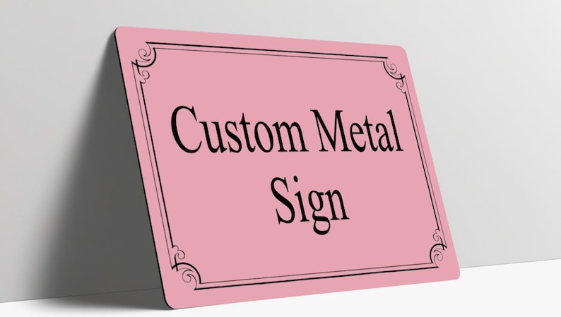 May include: A rectangular pink metal sign featuring a black border with decorative corner flourishes. The text Custom Metal Sign is printed in the center in a black serif font. The sign has rounded corners and a smooth, flat surface.