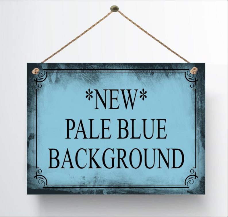 May include: A rectangular sign with a pale blue background and black text that reads "*NEW* PALE BLUE BACKGROUND". The sign has a dark border with decorative corner accents and is suspended by a brown rope.