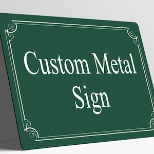 May include: A rectangular dark green metal sign with rounded corners. The sign features a white border with decorative corner flourishes and the white text Custom Metal Sign centered on the front surface of the flat metal plate.