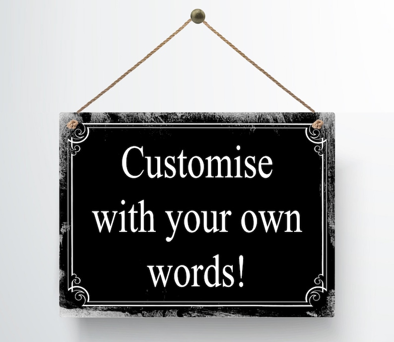 May include: A rectangular black sign with white text that reads "Customise with your own words!" The sign has a decorative white border and is suspended by a brown rope. The sign is hanging against a white background.
