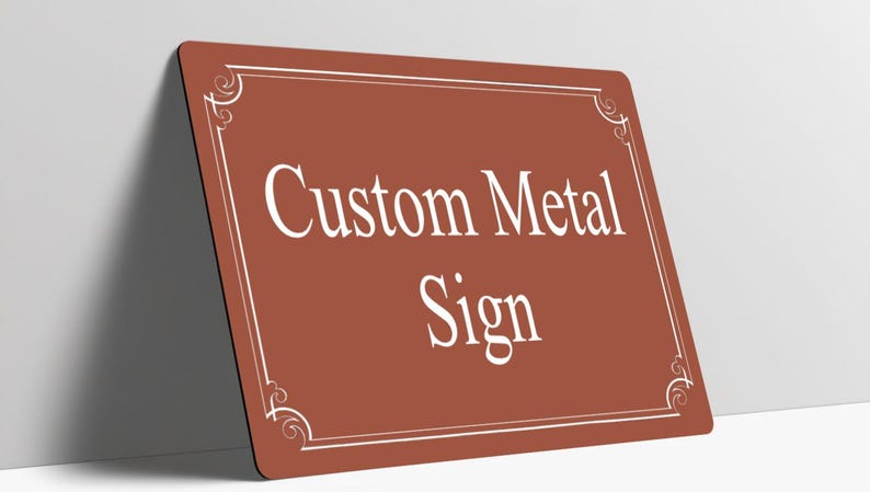 May include: A rectangular metal sign with a terracotta-colored background and rounded corners. The sign features a white border with decorative scrollwork at each corner and the white text Custom Metal Sign centered on the surface.