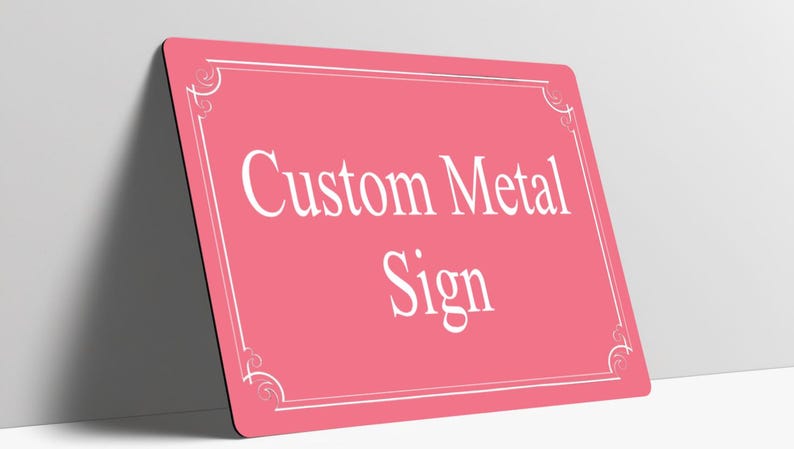 May include: A rectangular pink metal sign with rounded corners featuring a white border with decorative corner flourishes. The text Custom Metal Sign is printed in the center in a white serif font. The sign is positioned at an angle.
