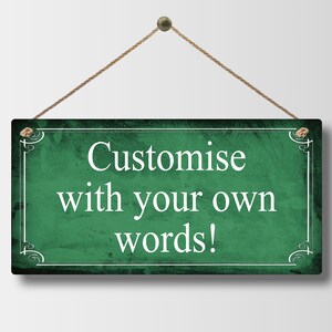 May include: A rectangular, dark green sign with white text that reads "Customise with your own words!" The sign is framed with a white border and decorative corner elements. It hangs from a natural rope.