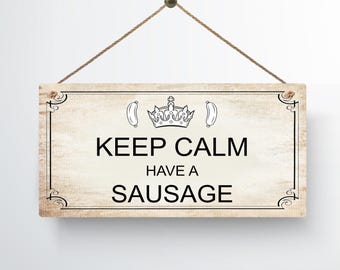 May include: A rustic wooden sign with a white background and black text that reads "Keep Calm Have A Sausage". The sign is decorated with a crown and two sausages.