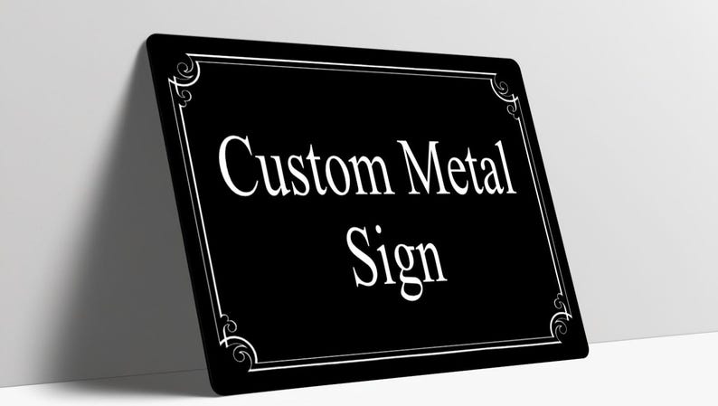 May include: A rectangular black metal sign with rounded corners featuring the white text Custom Metal Sign in a serif font. The sign has a thin white border with decorative scrollwork accents in each of the four corners.
