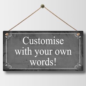 May include: A rectangular, dark gray sign with white text that reads "Customise with your own words!". The sign is framed with a white border and decorative corner elements. It hangs from a brown rope.