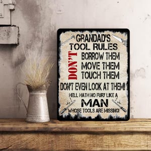 May include: A black and white metal sign with the text "Grandad's Tool Rules" and a list of rules: "Don't Borrow Them, Move Them, Touch Them, Don't Even Look At Them! Hell Hath No Fury Like A Man Whose Tools Are Missing!"