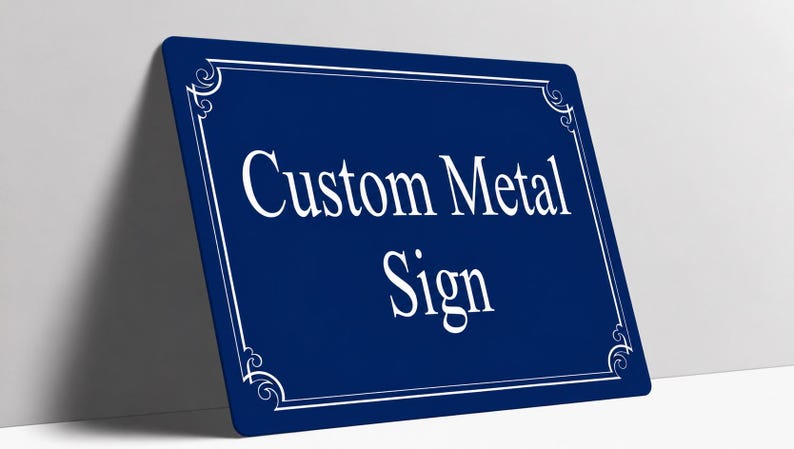 May include: A rectangular dark blue metal sign with rounded corners. The sign features a white decorative border and the white text Custom Metal Sign centered on the surface. The sign is positioned at an angle against a plain white wall.