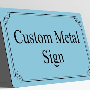 May include: A rectangular light blue metal sign with rounded corners and a black decorative border. The text Custom Metal Sign is printed in the center in a black serif font. The sign is positioned at an angle against a plain surface.
