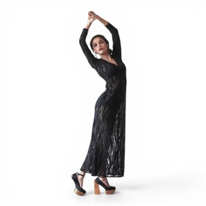 May include: A black, long-sleeved dress with a V-neck and a textured, open-weave design. The dress is paired with black platform heels with wooden block heels. The model is posing with arms raised.