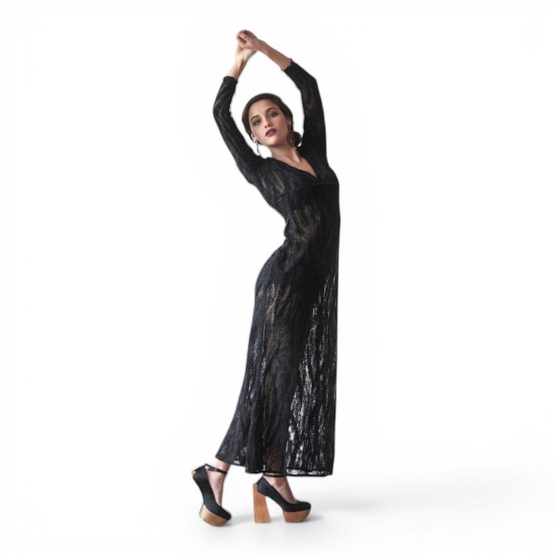 May include: A black, long-sleeved dress with a V-neck and a textured, open-weave design. The dress is paired with black platform heels with wooden block heels. The model is posing with arms raised.