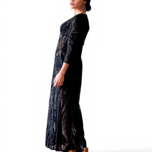 May include: A black lace maxi dress with long sleeves. The dress has a V-neckline and a flowing skirt. The model is wearing black platform shoes with wooden heels. The background is white.