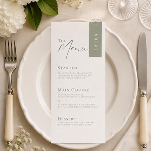 Peut inclure: Une carte de menu verticale blanche avec du texte noir et une bande décorative vert sauge portant le nom LAURA. Le menu détaille des plats incluant de la burrata fraîche, un filet de bœuf, du bar poêlé et une tarte au chocolat noir.