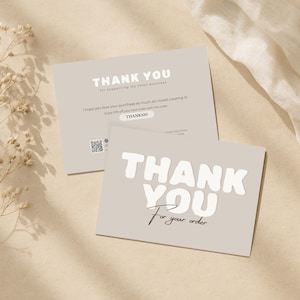 Op de afbeelding: Twee lichtgrijze bedankkaarten met witte tekst. Eén kaart leest "THANK YOU For your order" in een vetgedrukte lettertype. De andere kaart leest "THANK YOU for supporting my small business". Een QR-code en een kortingscode zijn ook zichtbaar.