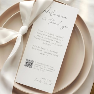 May include: A wedding reception place setting with a white card that reads "Welcome & thank you". The card is tied with a white ribbon and rests on a beige plate. A gold fork and knife are on either side.