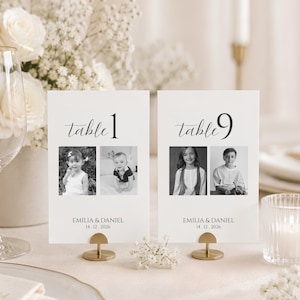 May include: Two white rectangular table number cards featuring the text table 1 and table 9, each displaying two black and white photographs of children, the names EMILIA & DANIEL, and the date 14.12.2026, held by small gold metal stands.