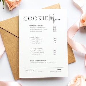 May include: A white rectangular menu card titled COOKIE Menu with black text listing individual cookies, cookie packs, and specialty cookies with prices. The card rests on a brown envelope, surrounded by light pink roses and a matching ribbon.