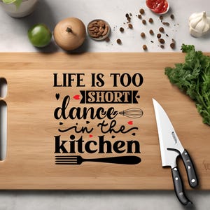 May include: A wooden cutting board with the text "Life is too short, dance in the kitchen" in black lettering with red hearts. A fork and whisk are also included in the design. A silver knife is lying on the board.