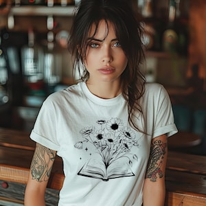 May include: A white t-shirt with a black and white graphic of an open book with flowers growing out of it.