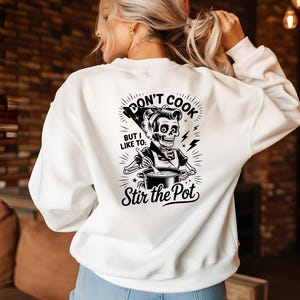 May include: White sweatshirt with a black and white graphic on the back. The graphic features a skeleton chef stirring a pot, with the text "Don't Cook But I Like To: Stir the Pot."