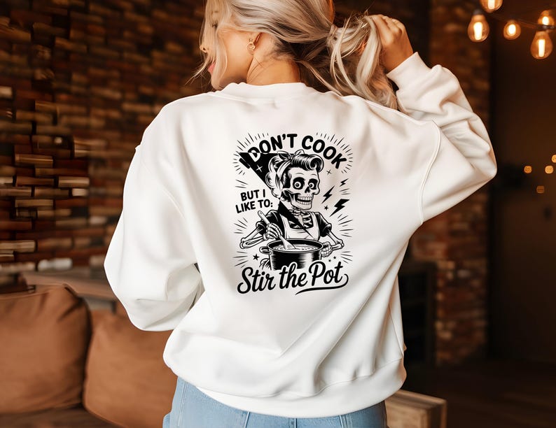 May include: White sweatshirt with a black and white graphic on the back. The graphic features a skeleton chef stirring a pot, with the text "Don't Cook But I Like To: Stir the Pot."