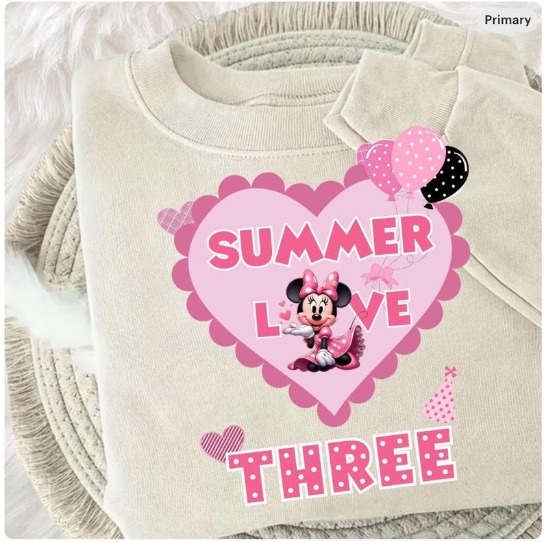 May include: A cream-coloured sweatshirt with a pink heart design. The heart features the words "SUMMER LOVE" and a Minnie Mouse graphic. The word "THREE" is below. Pink and black polka dot balloons and a party hat are also visible.
