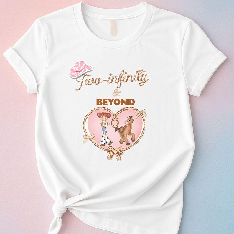 Peut inclure: T-shirt blanc avec un chapeau de cow-boy rose et l'inscription "Two-infinity & Beyond" en marron. Un motif en forme de c&oelig;ur comprend une cowgirl de dessin anim&eacute; et un cheval marron, encadr&eacute; par une bordure en corde.