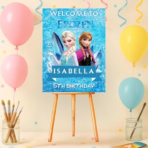 May include: A wooden easel holds a blue sign featuring Elsa and Anna from Frozen, with the text "Welcome to Frozen." The sign is for "Isabella's 5th Birthday." Pink, yellow, and blue balloons and paintbrushes decorate the scene.