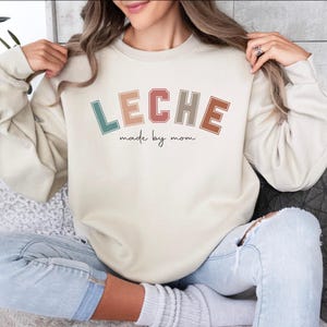 May include: A cream colored sweatshirt with the text "LECHE made by mom" in colorful retro lettering.