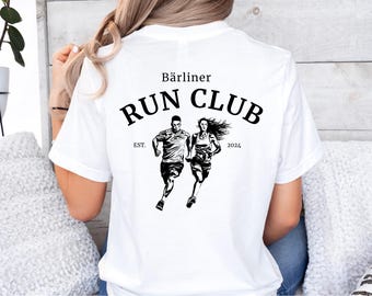 May include: White t-shirt with a black graphic of two runners and the text "Bärliner Run Club EST. 2024". The design features a male and female runner in motion, ideal for running enthusiasts.