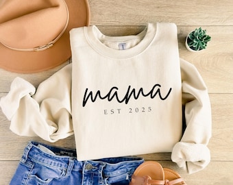 May include: A cream-colored sweatshirt with the text "mama est 2025" in black.