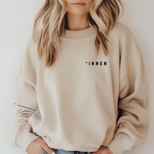 Pode incluir: Uma camisa de moletom bege com a palavra "*INNEN" impressa na frente.