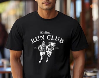 May include: Black t-shirt featuring a white graphic of two runners and the text "Bärliner Run Club" with "EST. 2024". The shirt is made of a soft material and is suitable for running or casual wear.