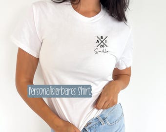 May include: White t-shirt featuring a small black emblem on the chest with crossed lines, letters, numbers, and a name in script. The text "Personalisierbares Shirt" is displayed on a blue rectangle.