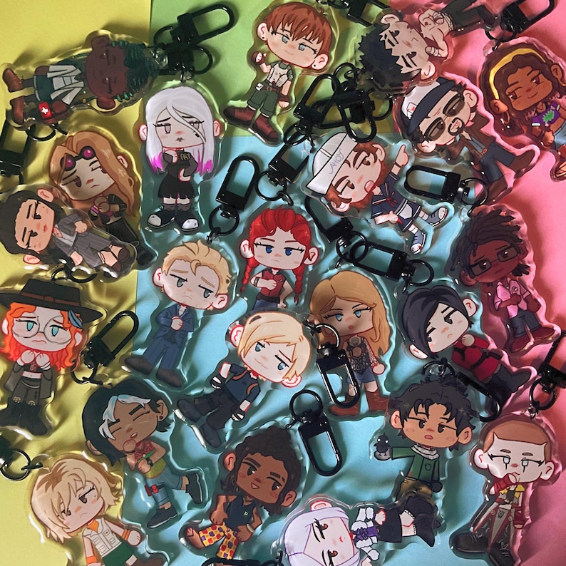 Puede incluir: Una colecci&oacute;n de llaveros acr&iacute;licos con varios personajes de dibujos animados. Cada llavero tiene un cierre negro y representa un personaje diferente con atuendos y peinados &uacute;nicos. Los llaveros est&aacute;n dispersos sobre un fondo colorido.