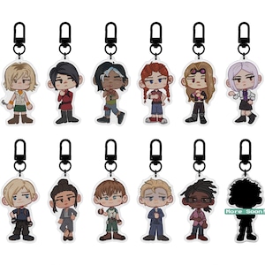Puede incluir: Una colecci&oacute;n de llaveros de personajes con mosquetones negros. Cada llavero presenta un dise&ntilde;o &uacute;nico de personaje de dibujos animados con varios atuendos y peinados. La frase "More Soon!" es visible en un llavero.