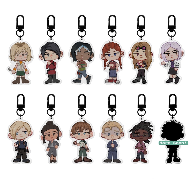 Puede incluir: Una colecci&oacute;n de llaveros de personajes con mosquetones negros. Cada llavero presenta un dise&ntilde;o &uacute;nico de personaje de dibujos animados con varios atuendos y peinados. La frase "More Soon!" es visible en un llavero.