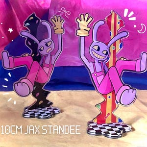 Puede incluir: Dos figuras acrílicas Jax de 10 cm que muestran un personaje de conejo morado con overol rosa y guantes amarillos. Una figura muestra al personaje con expresión preocupada sobre fondo negro, mientras que la otra muestra una sonrisa sobre fondo a rayas.