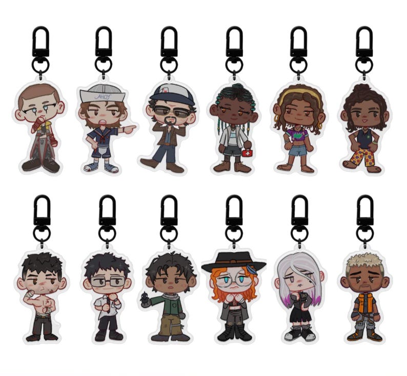 Puede incluir: Una colecci&oacute;n de llaveros tem&aacute;ticos de personajes. Cada llavero presenta una ilustraci&oacute;n de dibujos animados de una persona con atuendos y accesorios &uacute;nicos. Los llaveros est&aacute;n sujetos a cierres de metal negro.