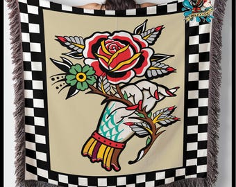 May include: A woven throw blanket with a checkered black and white border. The center features a vintage tattoo style illustration of a hand holding a red rose with green leaves and thorns.