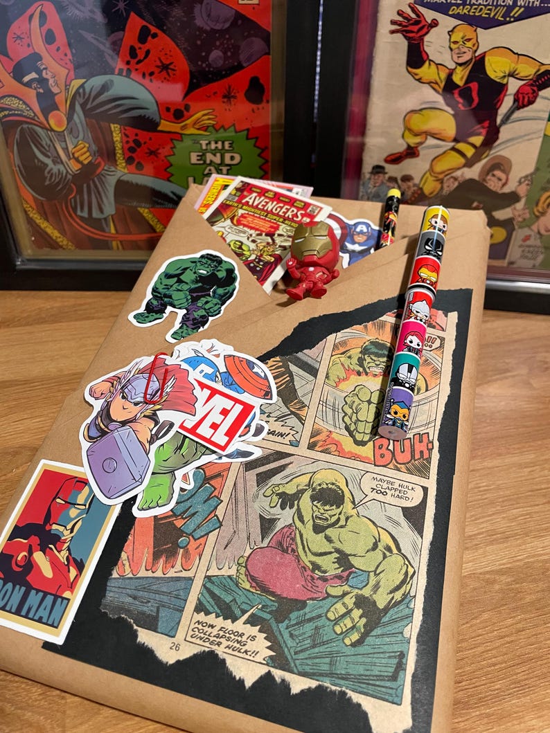 May include: A brown paper gift bag decorated with comic book characters, including Hulk, Thor, Iron Man, and the Avengers. The bag has a pencil with a superhero character design on it.