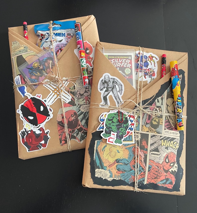 May include: Two brown paper packages wrapped with twine and decorated with comic book character stickers. The packages are tied with twine and have a variety of stickers featuring characters like Spiderman, Hulk, and Deadpool.