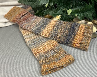 May include: A pair of hand-knitted leg warmers featuring a variegated yarn pattern in shades of burnt orange, charcoal gray, and cream. The knit fabric has a ribbed texture at the top and bottom edges, showcasing a consistent, chunky stitch.