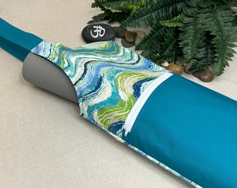 May include: A teal yoga mat carrier with a zippered pocket. The carrier is made of a teal fabric with a white and blue marbled pattern. The carrier has a teal strap.